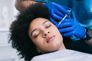 Attractive young African woman is getting a rejuvenating facial injections. She is sitting calmly at clinic.